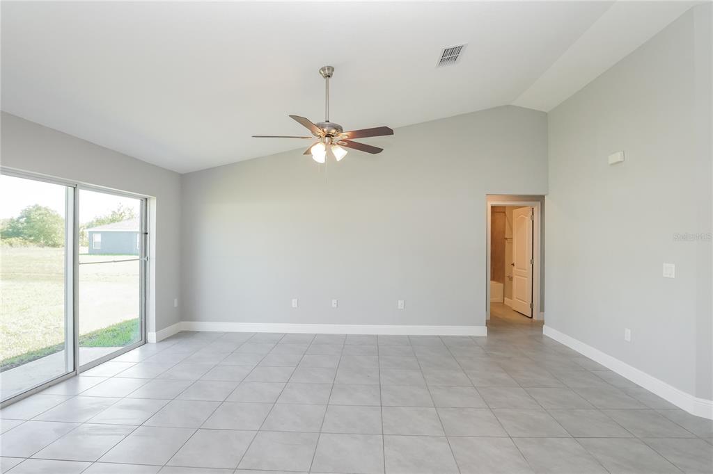 A spacious living room with light gray walls, tile flooring, a vaulted ceiling, and sliding doors — 286 BECKENHAM DRIVE, KISSIMMEE, FL