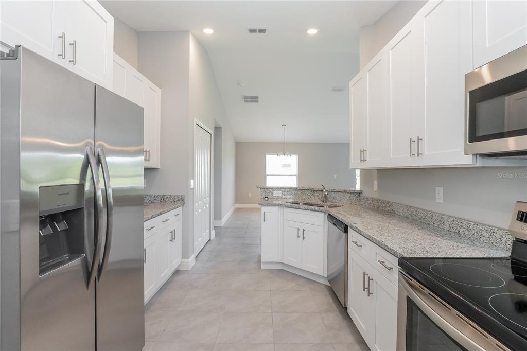 A kitchen features white cabinets, granite countertops, stainless steel appliances, and light gray floor tiles — 286 BECKENHAM DRIVE, KISSIMMEE, FL