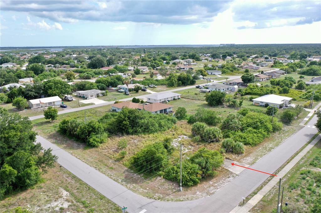 An aerial view shows a vacant, brush-covered corner lot with a small concrete driveway entrance — 27147 SUNNYBROOK ROAD, PUNTA GORDA, FL