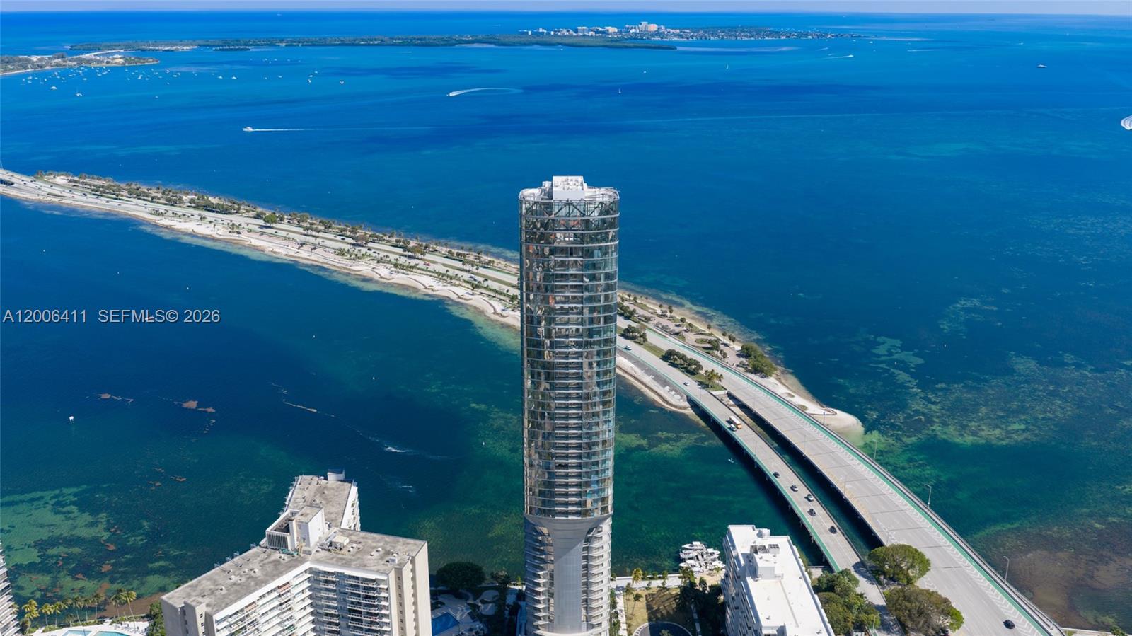 An aerial view shows a tall, cylindrical glass skyscraper situated next to a coastal highway — 175 SE 25th Road # 1202, Miami FL 33129, MIAMI, FL