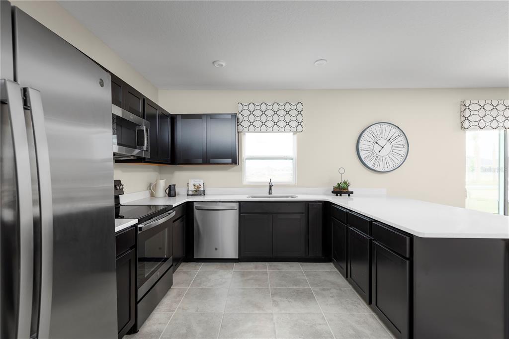 A kitchen features dark cabinets, stainless steel appliances, white countertops, and light tile flooring — 11464 SE 77TH AVENUE, BELLEVIEW, FL