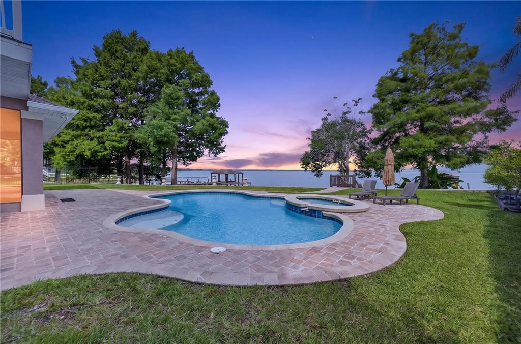 A backyard features a swimming pool with a spa overlooking a lake at sunset — 279 ZACHARY WADE STREET, WINTER GARDEN, FL