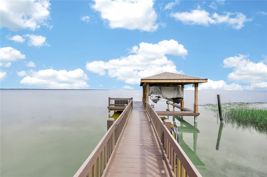 A wooden pier leads to a covered boat lift over calm water under a sky — 279 ZACHARY WADE STREET, WINTER GARDEN, FL