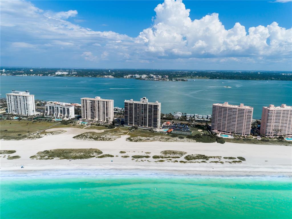 An aerial view of high-rise apartment buildings situated along a sandy beach and turquoise water — 1290 GULF BOULEVARD UNIT 907, CLEARWATER, FL