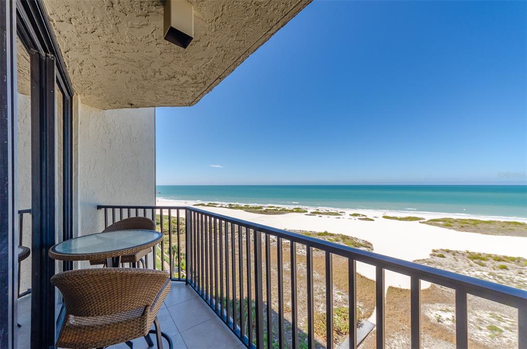 A balcony with a small table and chairs overlooks a sandy beach and the ocean — 1290 GULF BOULEVARD UNIT 907, CLEARWATER, FL