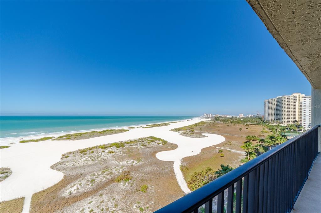 A high-angle view from a balcony overlooking a white sand beach and the ocean — 1290 GULF BOULEVARD UNIT 907, CLEARWATER, FL