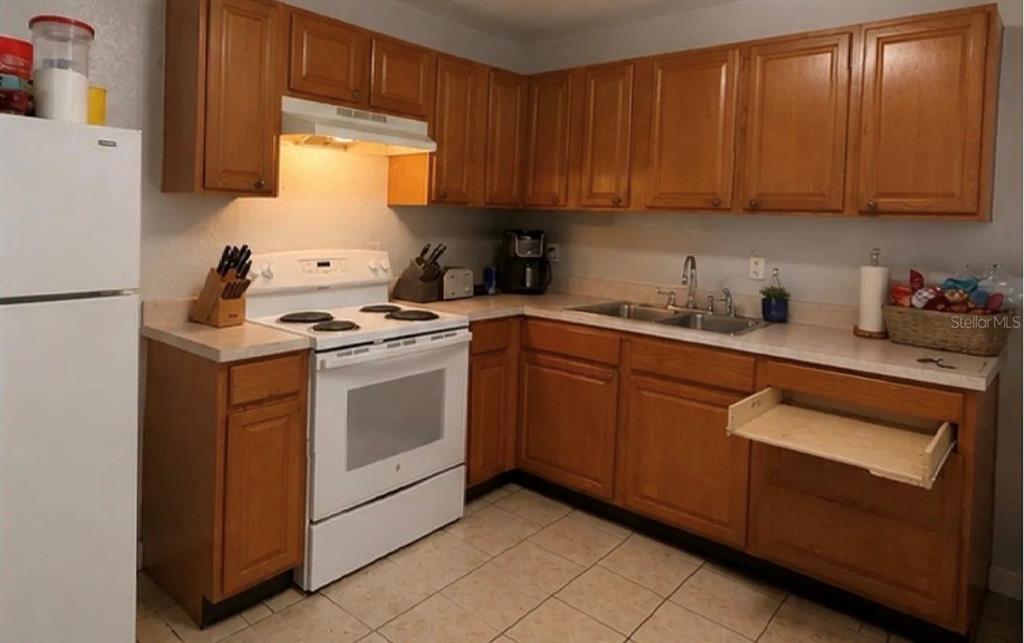 A kitchen features wood cabinets, white appliances, a double sink, and light-colored tile flooring — 107 LAKE ELIZABETH DRIVE UNIT B, WINTER HAVEN, FL
