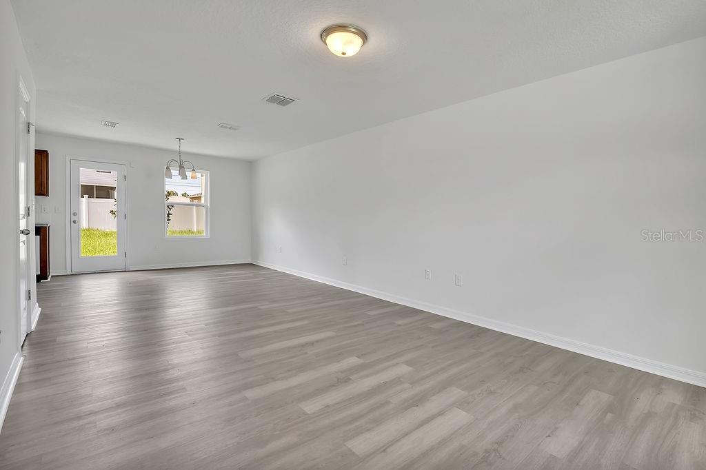 An empty living area features light wood-look flooring, white walls, and a glass-paned exterior door — 303 ANCHOVIE COURT, POINCIANA, FL