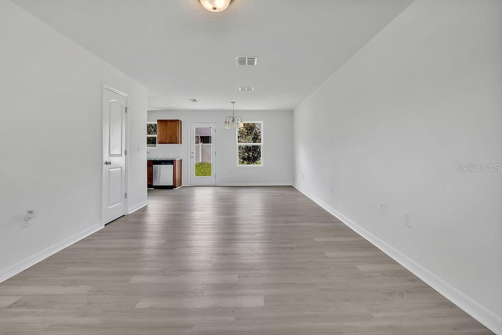 An open-concept living and dining area features light wood-look flooring and white walls — 303 ANCHOVIE COURT, POINCIANA, FL