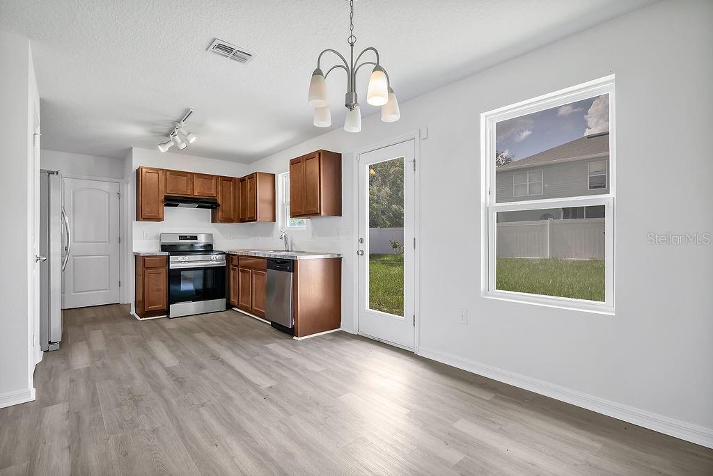 A kitchen with wood cabinets, stainless steel appliances, and light wood-look flooring — 303 ANCHOVIE COURT, POINCIANA, FL