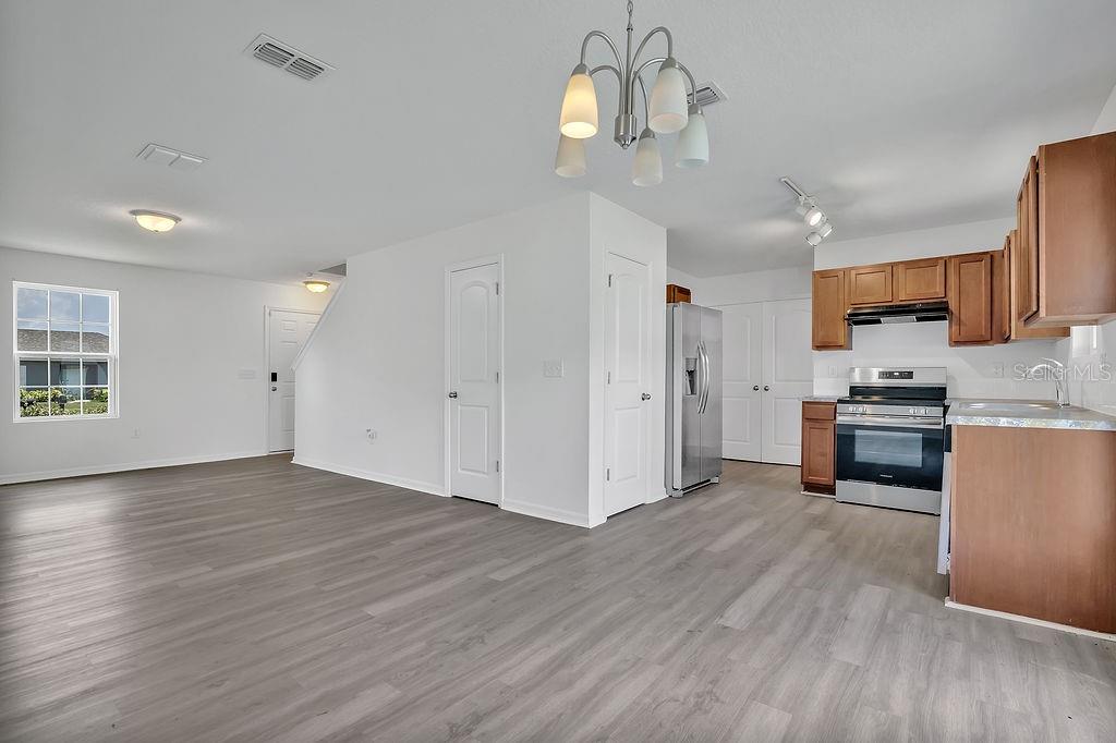 An open-concept kitchen and living area feature light wood-look flooring and white walls — 303 ANCHOVIE COURT, POINCIANA, FL
