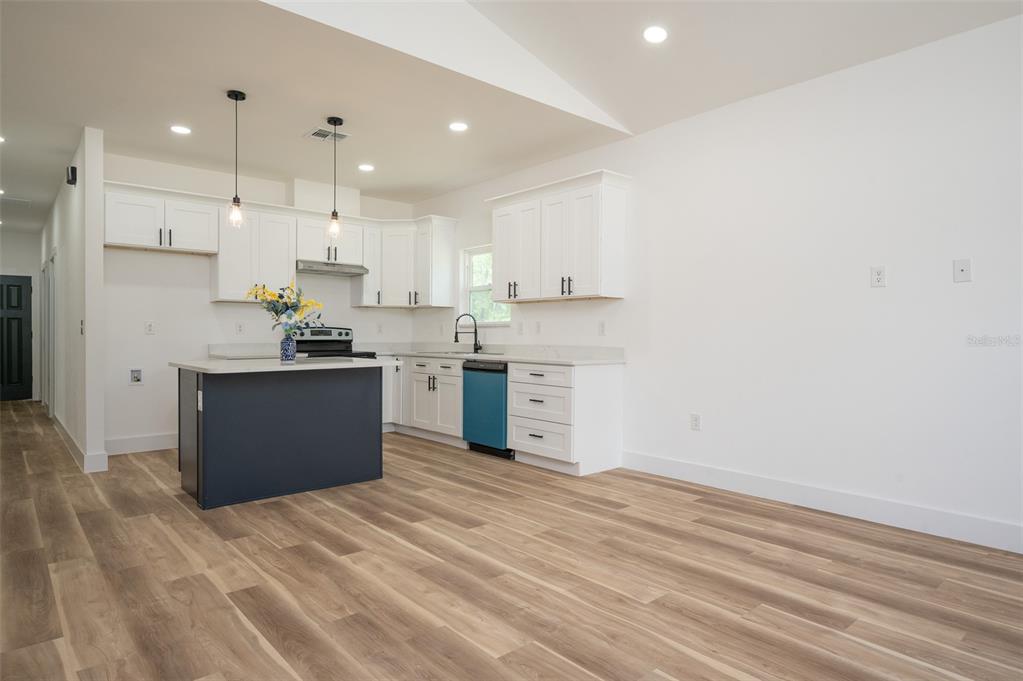 A modern kitchen features white cabinets, a dark blue island, and light wood-look flooring — 1510 NE 156TH TERRACE, WILLISTON, FL
