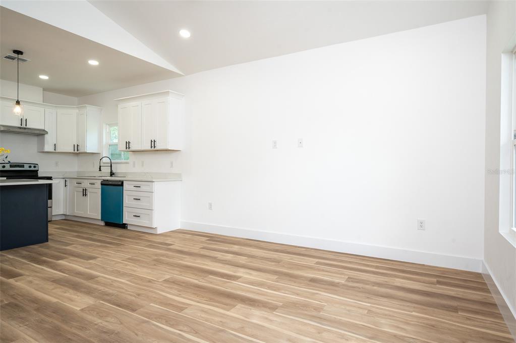 A bright, open-concept living area features white walls, light wood-look flooring, and an adjacent kitchen — 1510 NE 156TH TERRACE, WILLISTON, FL