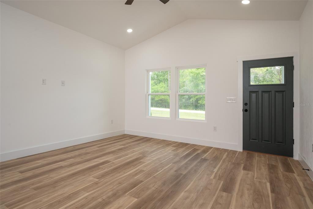 An empty room with white walls, wood-look flooring, a vaulted ceiling, and a dark door — 1510 NE 156TH TERRACE, WILLISTON, FL