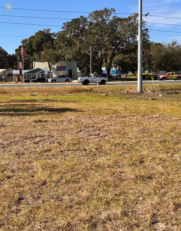 A vacant grassy lot sits in the foreground with a road and commercial buildings behind — S US HIGHWAY 27/441, LADY LAKE, FL