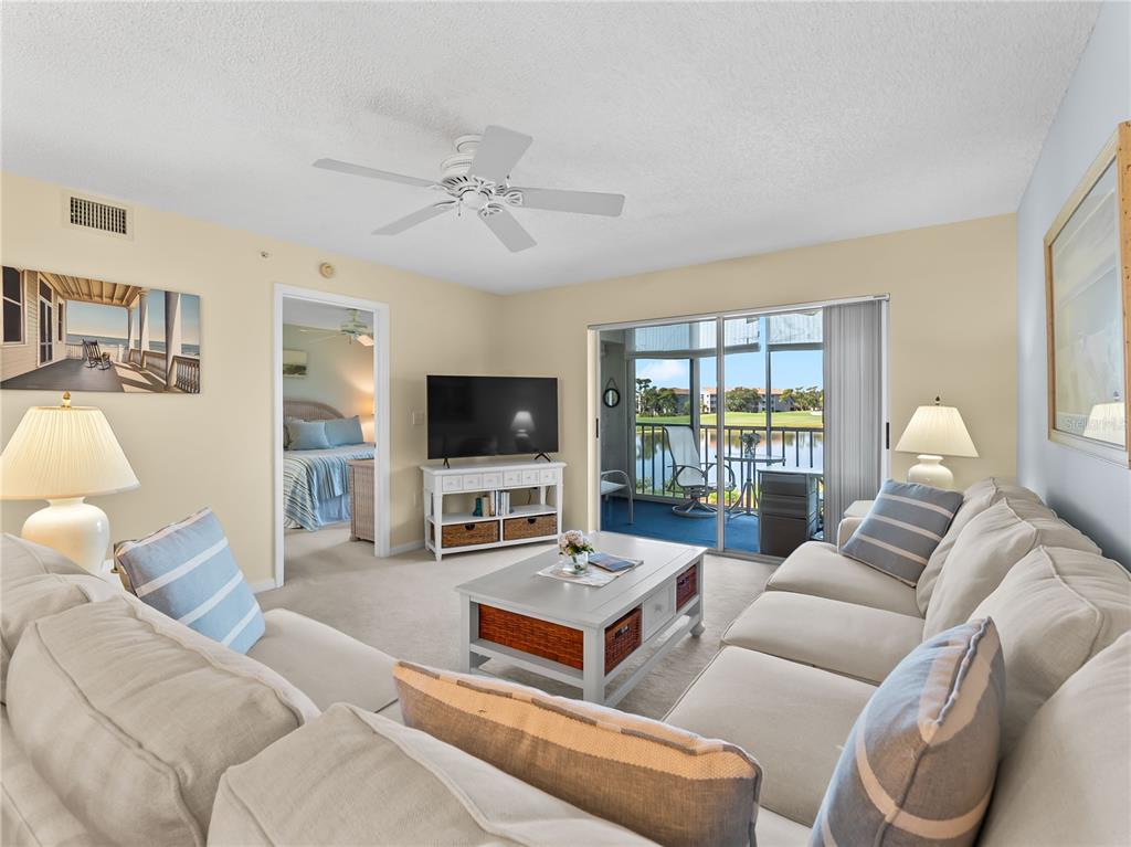 A living room features beige sofas, a coffee table, a television, and a sliding glass door — 9330 CLUBSIDE CIRCLE UNIT 3207, SARASOTA, FL