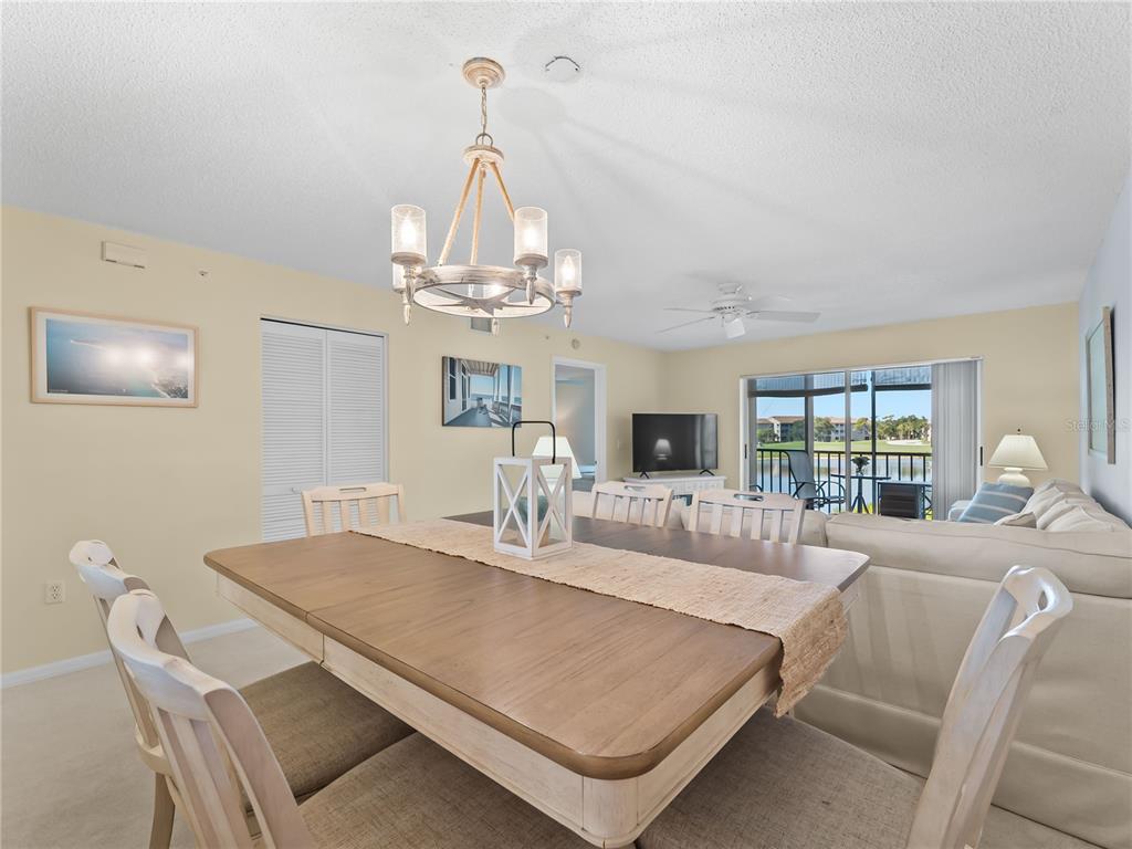 A dining area with a wooden table and chandelier opens into a living room space — 9330 CLUBSIDE CIRCLE UNIT 3207, SARASOTA, FL