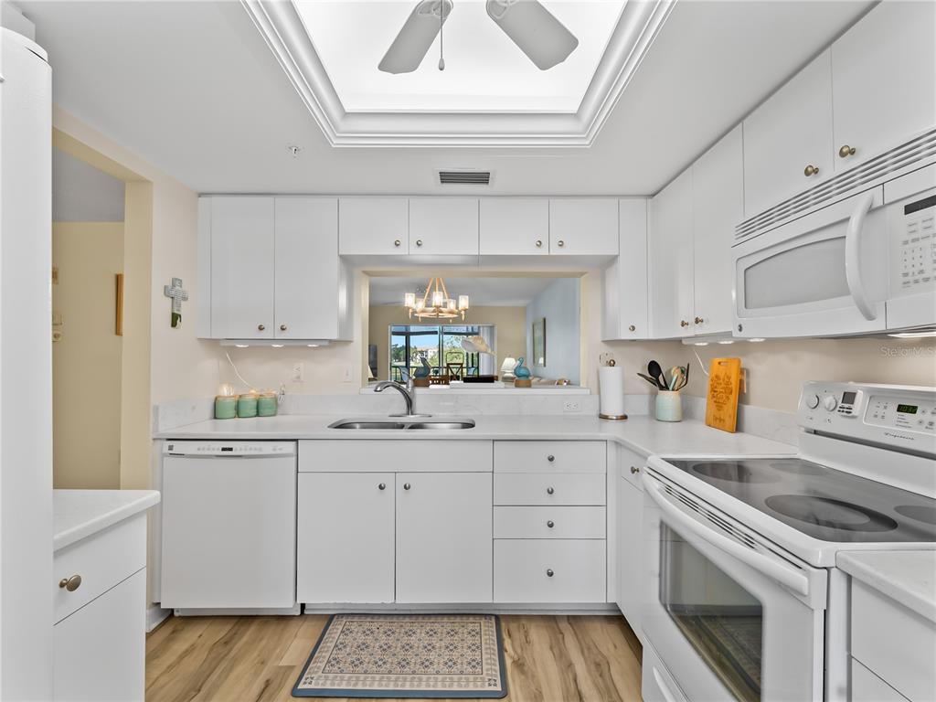 A white kitchen features light wood flooring, a skylight, and a pass-through window — 9330 CLUBSIDE CIRCLE UNIT 3207, SARASOTA, FL