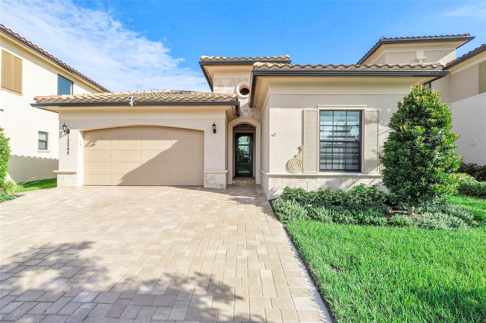 A beige stucco house features a paver driveway, a two-car garage, and a tiled roof — 12245 N Baypoint Circle, Parkland FL 33076, PARKLAND, FL