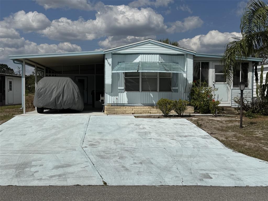 A light blue mobile home features a covered carport, a concrete driveway, and an awning — 8508 BREEZE HILL DRIVE, LAKE WALES, FL