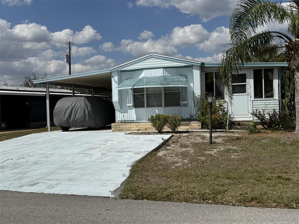 A light blue mobile home features a carport, a covered entrance, and a concrete driveway — 8508 BREEZE HILL DRIVE, LAKE WALES, FL