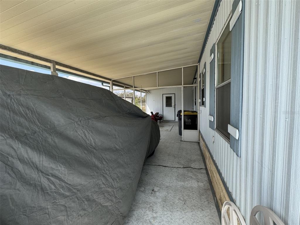 A covered carport area features a vehicle under a gray cover and a side door — 8508 BREEZE HILL DRIVE, LAKE WALES, FL
