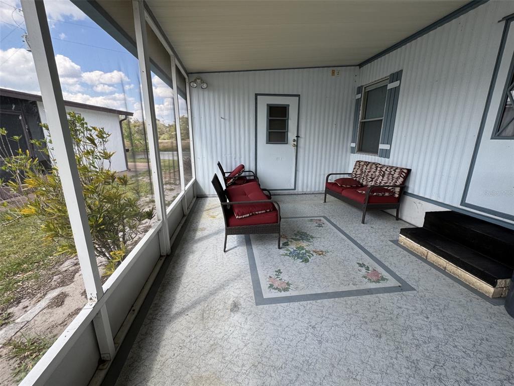 A screened-in porch features a patterned area rug, patio furniture, and white vertical siding — 8508 BREEZE HILL DRIVE, LAKE WALES, FL