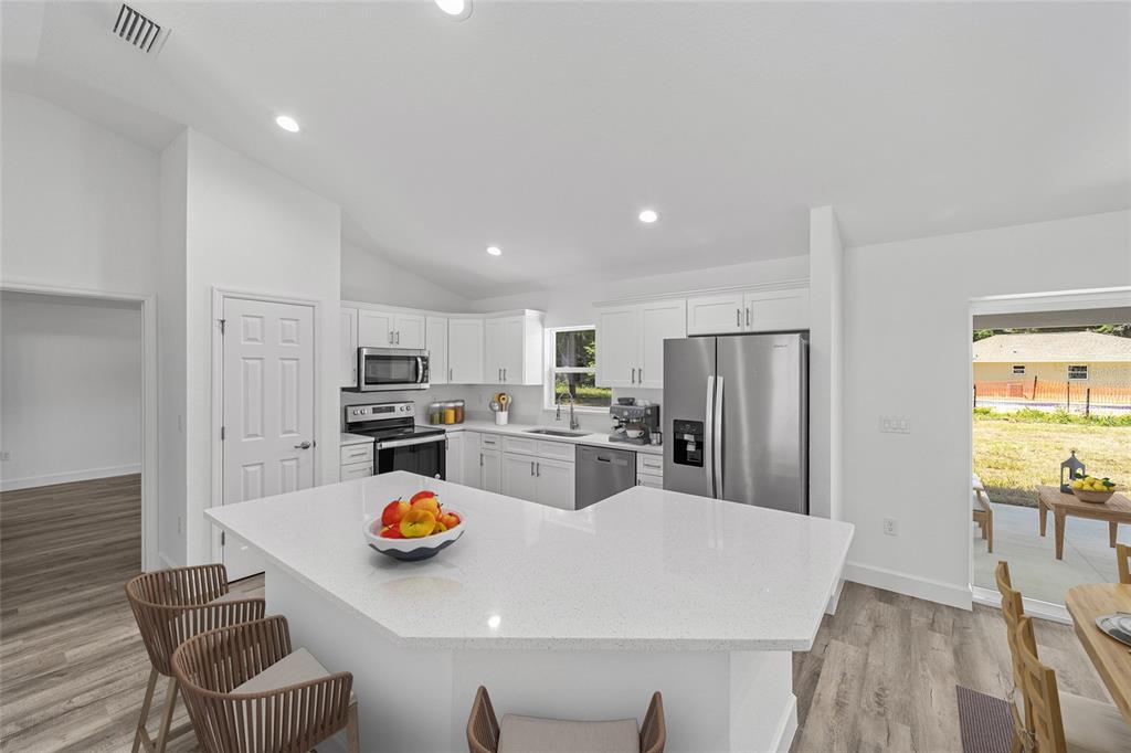 A white kitchen features a quartz-topped island, stainless steel appliances, and wood-look flooring — 6283 NW 61ST STREET, OCALA, FL