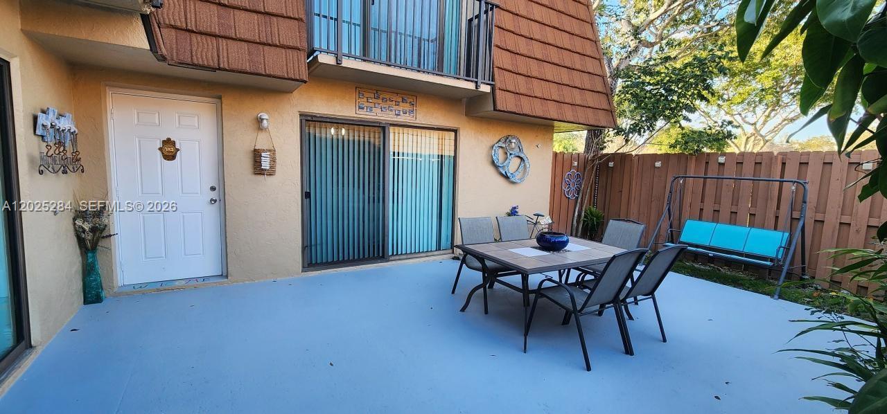 A patio features a dining set, a swing, and a white door against a building — COOPER CITY, FL