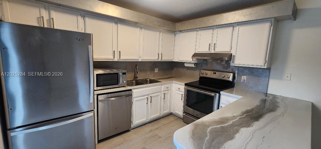 A kitchen features white cabinets, stainless steel appliances, and a gray-veined countertop peninsula — COOPER CITY, FL