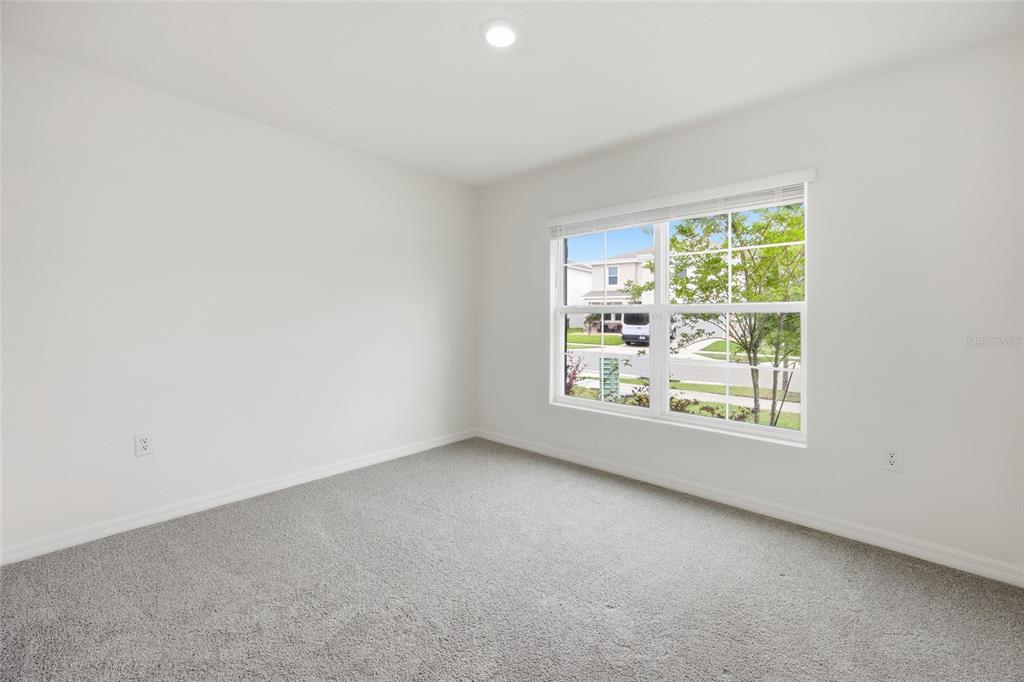 An empty bedroom features white walls, gray carpeting, and a window overlooking a suburban street — 5527 SW 43RD COURT, OCALA, FL
