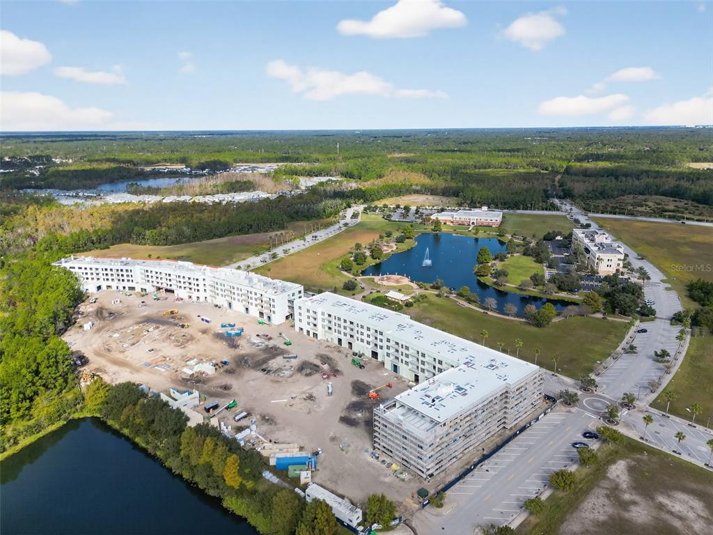 An aerial view shows a large multi-story building under construction near a pond and forest — 469 BULLDOG DRIVE UNIT 2, PALM COAST, FL