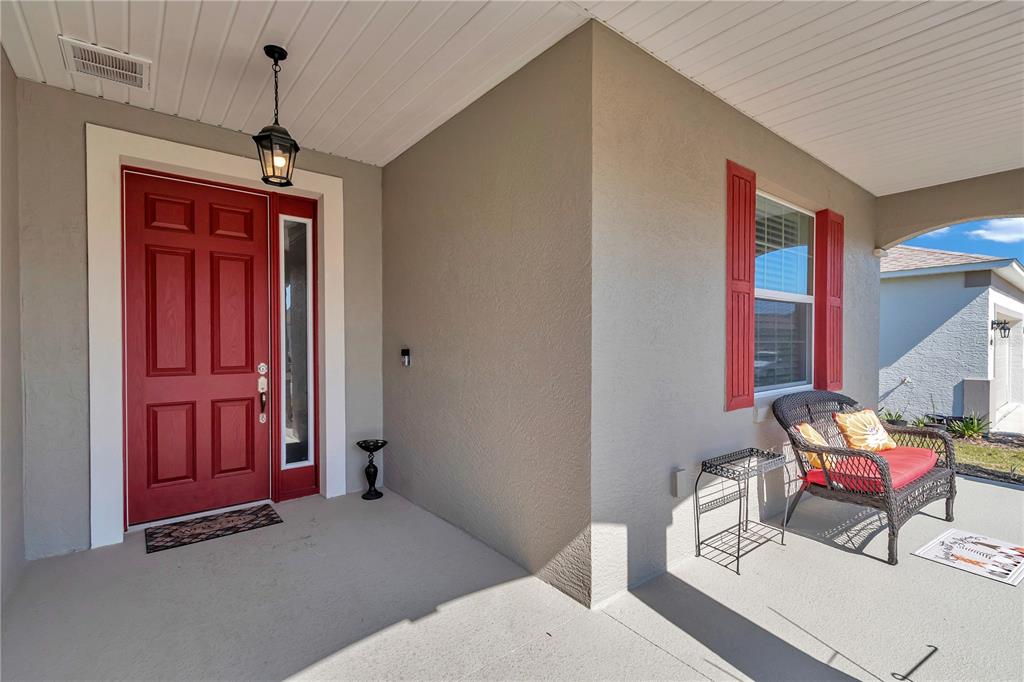 A covered front porch features a red door, a wicker chair, and a light fixture — 10019 SW 96TH STREET, OCALA, FL