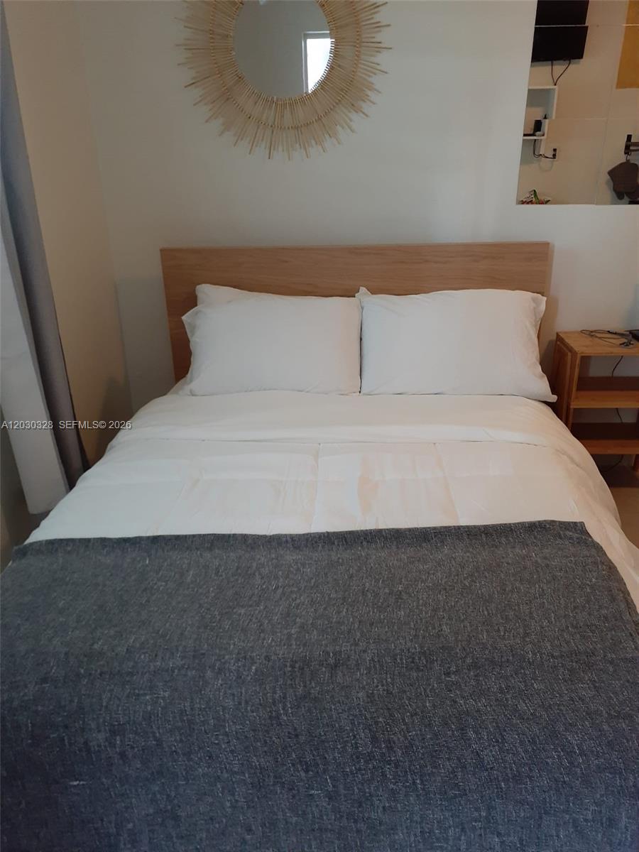 A bedroom features a bed with white bedding, a gray throw, and a wooden headboard — 2306 Sunshine Blvd, Miramar FL 33023, MIRAMAR, FL