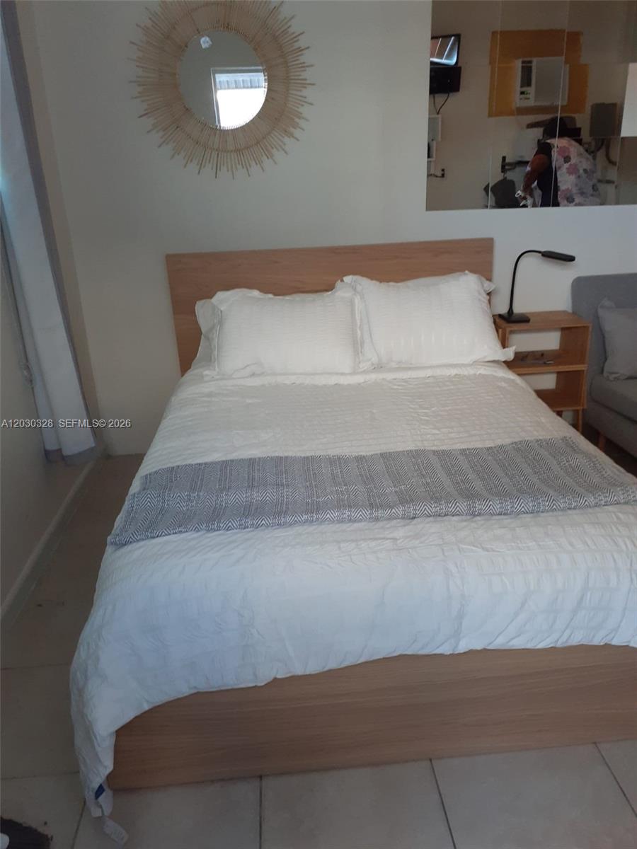 A bedroom features a light wood bed frame, white bedding, and a decorative sunburst mirror — 2306 Sunshine Blvd, Miramar FL 33023, MIRAMAR, FL
