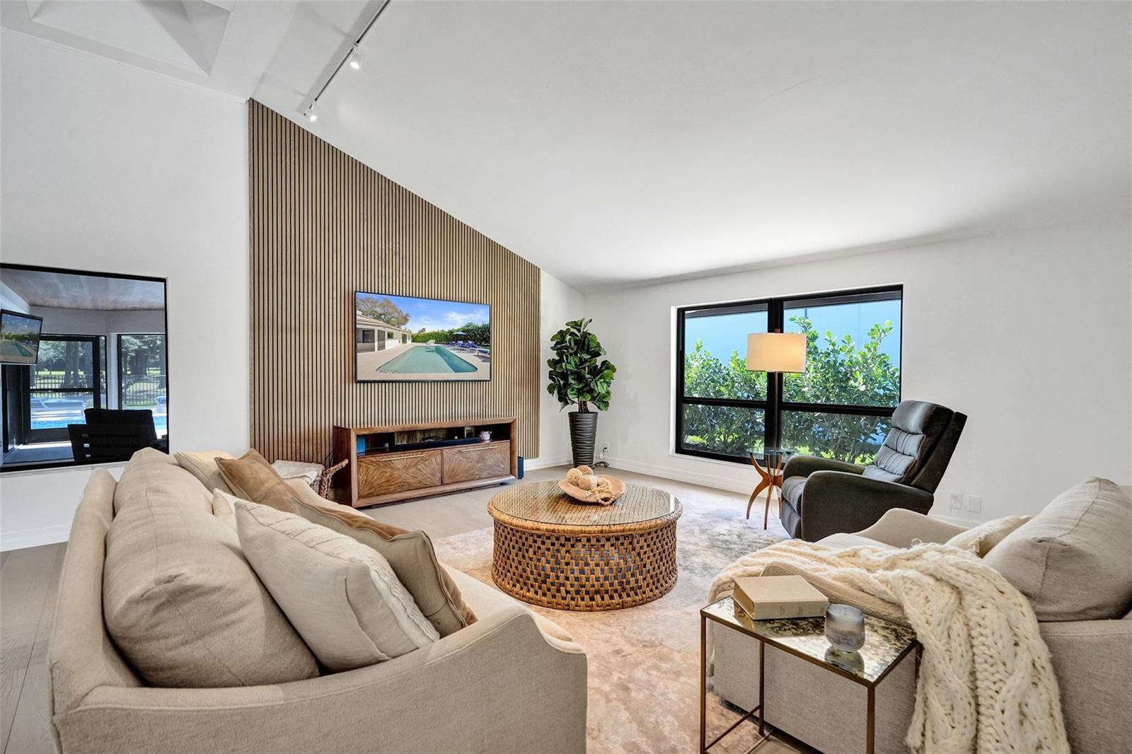 A living room features a slatted wood accent wall, a television, and a round table — 614 Lakewoode Circle W, Delray Beach FL 33445, DELRAY BEACH, FL