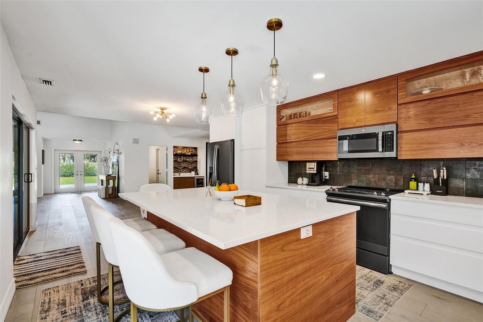 A modern kitchen features a large white island, wood cabinetry, and stainless steel appliances — 614 Lakewoode Circle W, Delray Beach FL 33445, DELRAY BEACH, FL