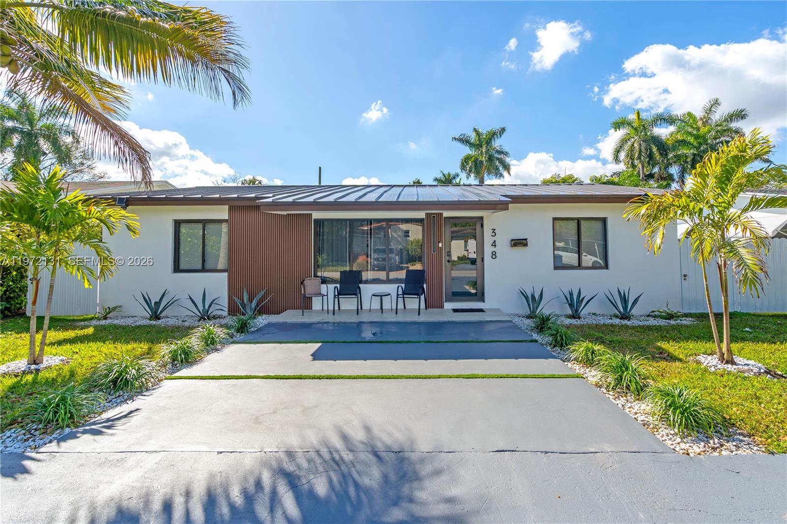 A single-story house with a metal roof, wood-slat accent wall, and a concrete driveway — 348 NE 117th St, Miami FL 33161, MIAMI, FL