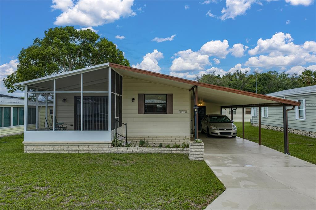 A single-story manufactured home with a screened-in porch, a carport, and light-colored siding — 35116 COLONY HILLS DRIVE, ZEPHYRHILLS, FL