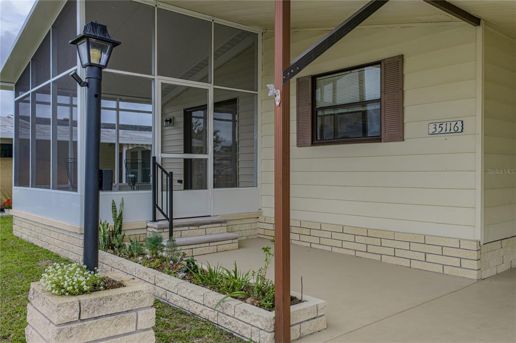 A tan mobile home features a screened-in porch, a brick planter, and a front entrance — 35116 COLONY HILLS DRIVE, ZEPHYRHILLS, FL