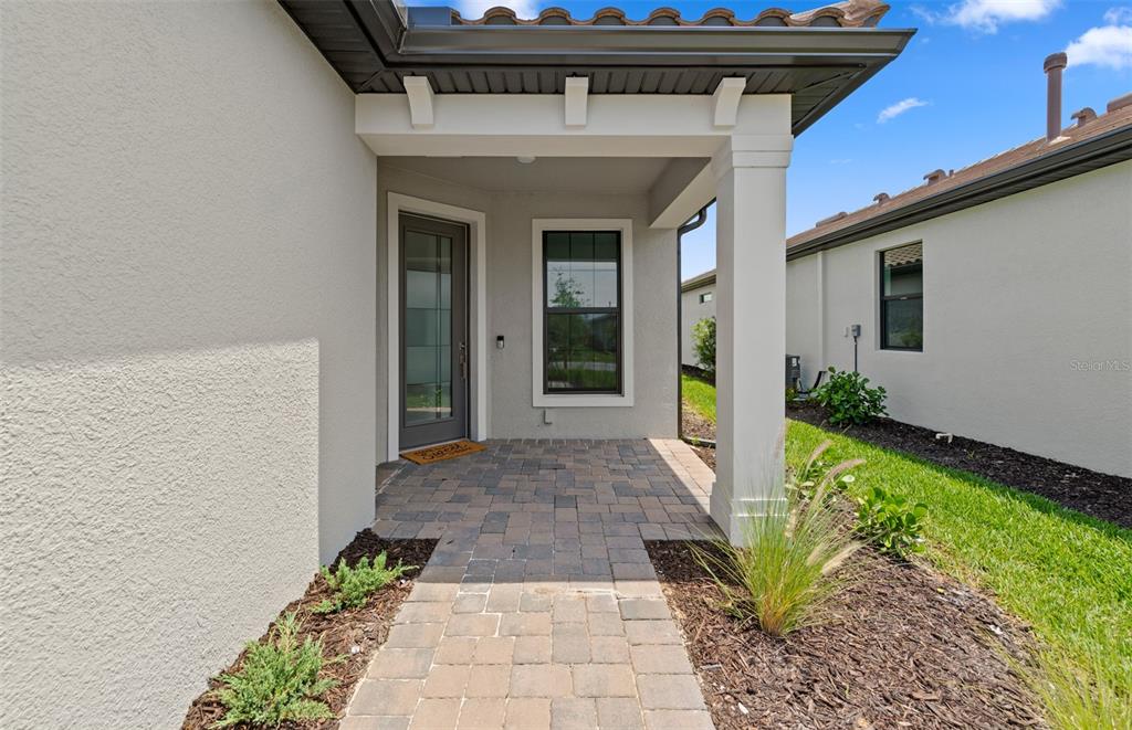 A paved walkway leads to the front entrance of a house with a covered porch — 5834 TALON PRESERVE DRIVE, NOKOMIS, FL