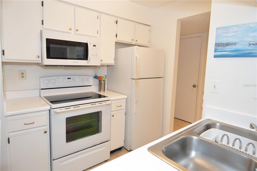 A kitchen features white cabinets, white appliances, a stainless steel sink, and a tiled floor — 8625 MALLARD RESERVE DRIVE UNIT 101, TAMPA, FL