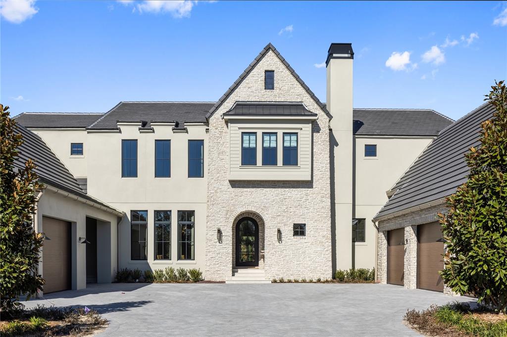 A large two-story house with a stone facade, dark roof, and a paved driveway — 9323 GLADYS GARDEN COURT, WINDERMERE, FL
