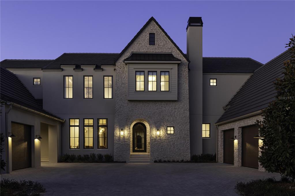 A large, two-story stone and stucco house with a paved driveway at dusk — 9323 GLADYS GARDEN COURT, WINDERMERE, FL