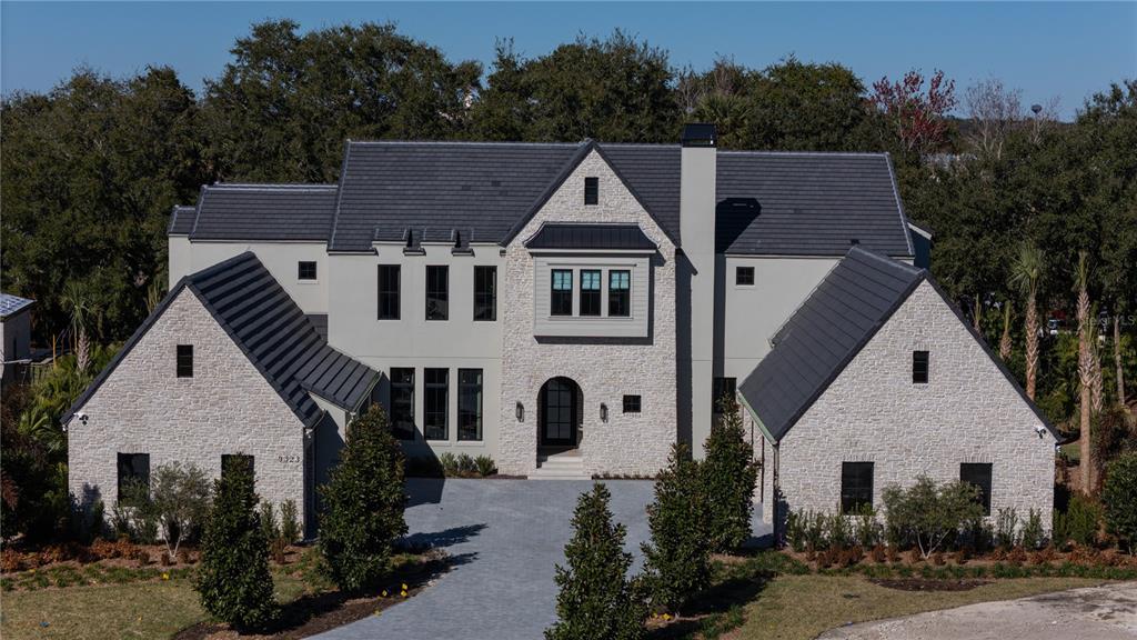 An exterior view of a large, two-story house with stone siding and a dark roof — 9323 GLADYS GARDEN COURT, WINDERMERE, FL