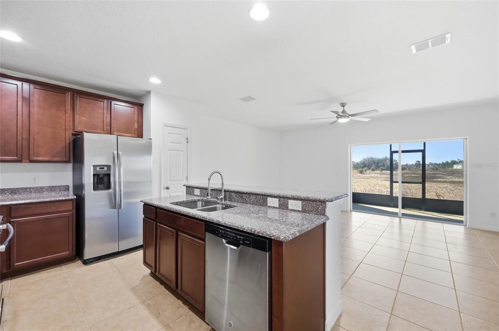 A kitchen with dark wood cabinets, granite countertops, and stainless steel appliances overlooks a living area — 196 PRIMROSE DRIVE, DAVENPORT, FL