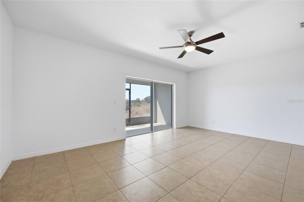 A bright room with white walls, tan tile flooring, a ceiling fan, and sliding glass doors — 196 PRIMROSE DRIVE, DAVENPORT, FL