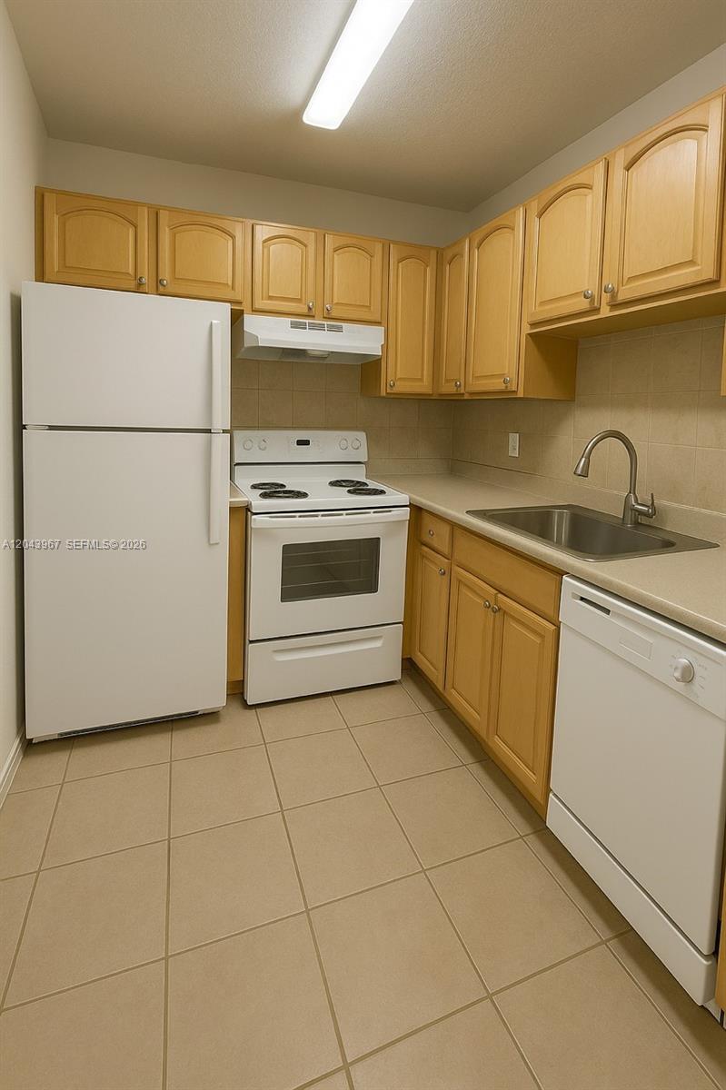 A kitchen features light wood cabinets, white appliances, and beige tile flooring — 2775 Taft St # 307, Hollywood FL 33020, HOLLYWOOD, FL