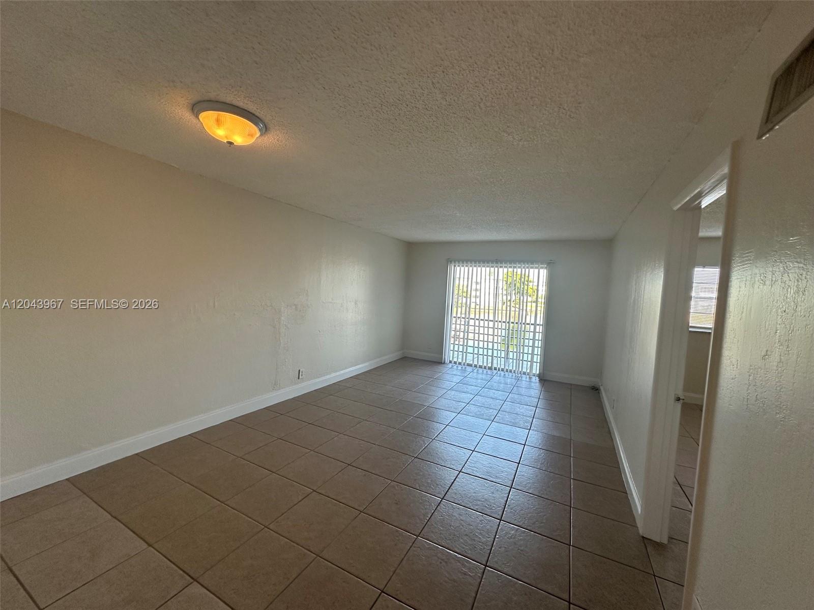 An empty room features beige tile flooring, light-colored walls, a ceiling light, and vertical blinds — 2775 Taft St # 307, Hollywood FL 33020, HOLLYWOOD, FL