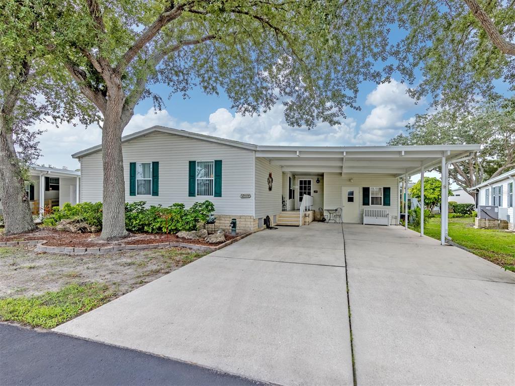 A single-story manufactured home with a concrete driveway, carport, and mature trees in the yard — 213 NATURES WAY, NORTH PORT, FL